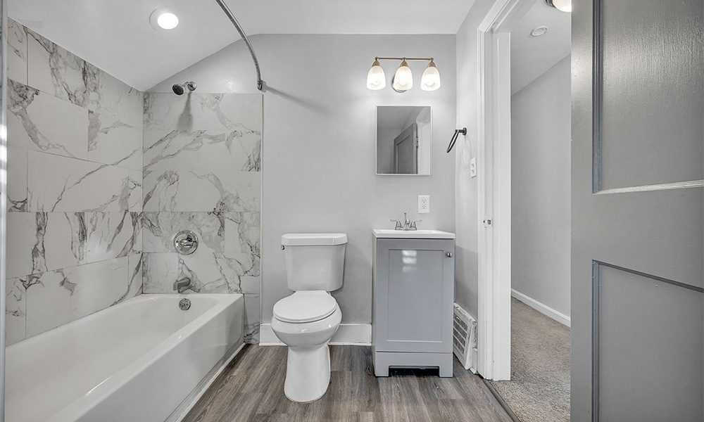 Renovated bathroom with marble-style tiled tub surround