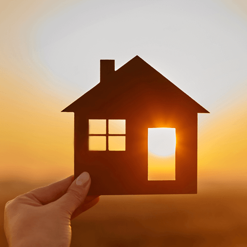 someone holds a handmade figure of a house up to a sunset