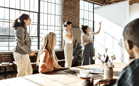 a team of co-workers are stood around a whiteboard